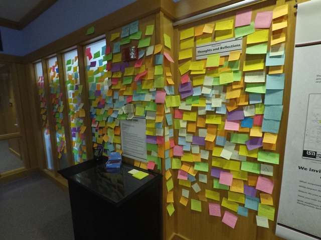 A wall covered in Post-It Notes with comments from exhibit viewers.