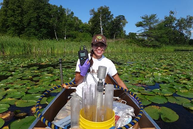 Person in canoe gathering water samples in a lake.
