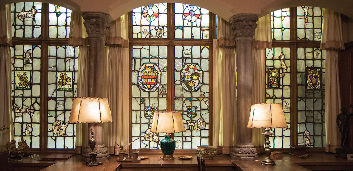 One side of the Bell Period Room with three stained glass windows and three lit lamps 