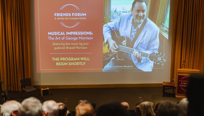 Image projected on a screen portraying the event's featured performer, Briand Morrison. Audience visible in foreground.