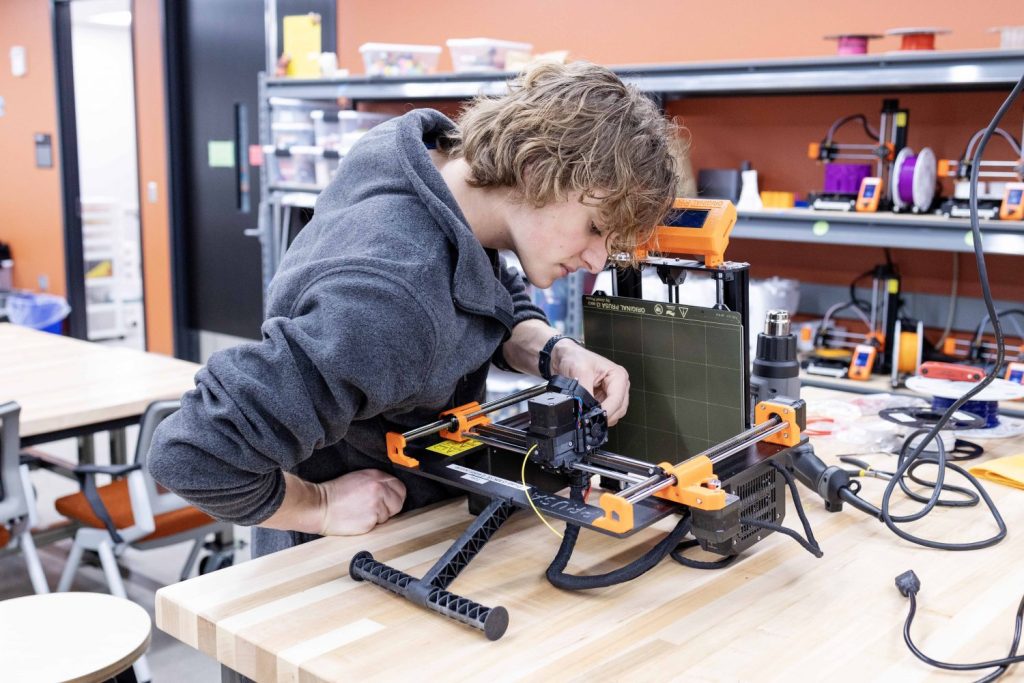 Student operating a 3D printer atop a desk.