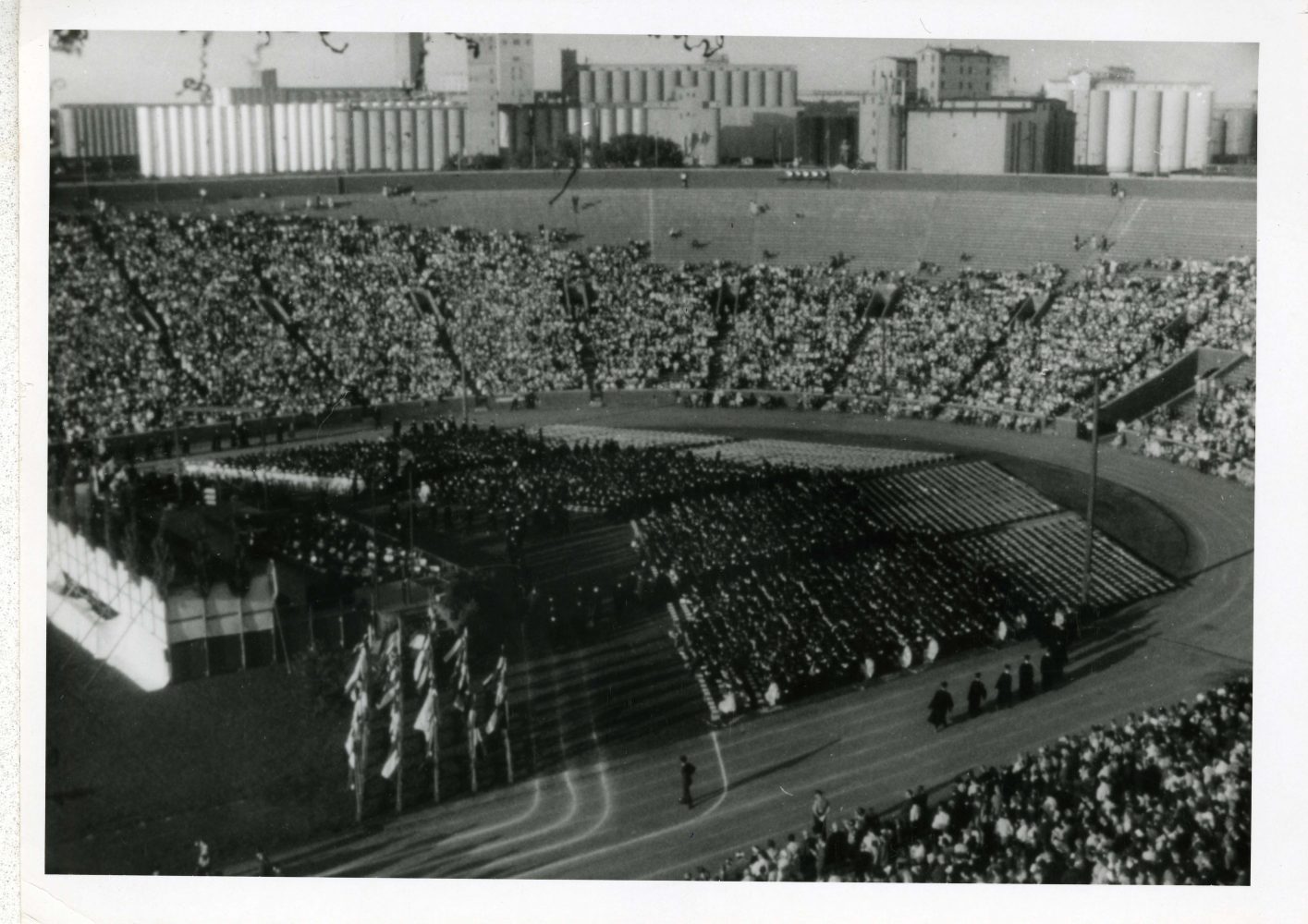 Graduates sit in chairs on the field of Memorial Stadium in front of a stage. Attendees are in the stadium bleachers.