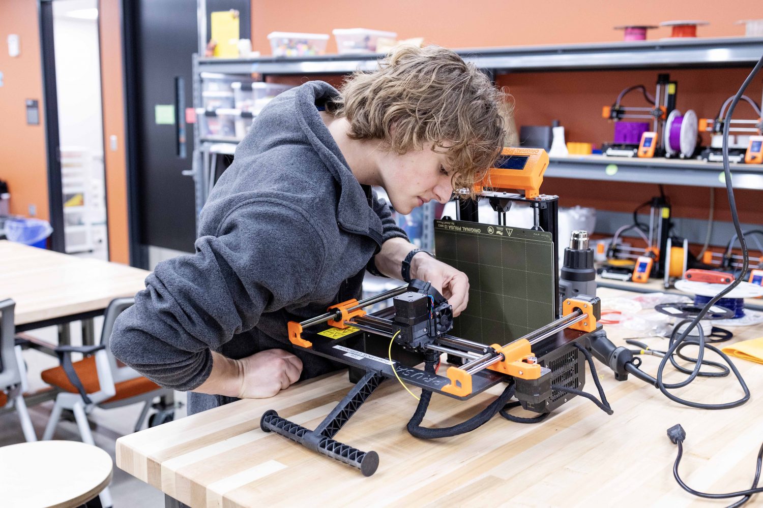 Student operating a 3D printer atop a desk.