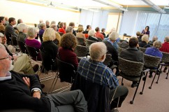 An image of a large room filled with people hearing a speaker celebrate the 50th anniversary of the IHRC/A.