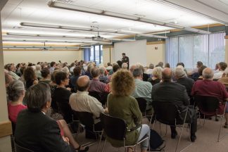 Prof. John S. Wright speaking to a crowded room about the exhibit.