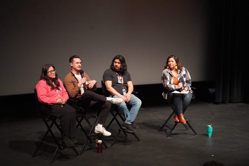A host and three panelists sit on a stage.