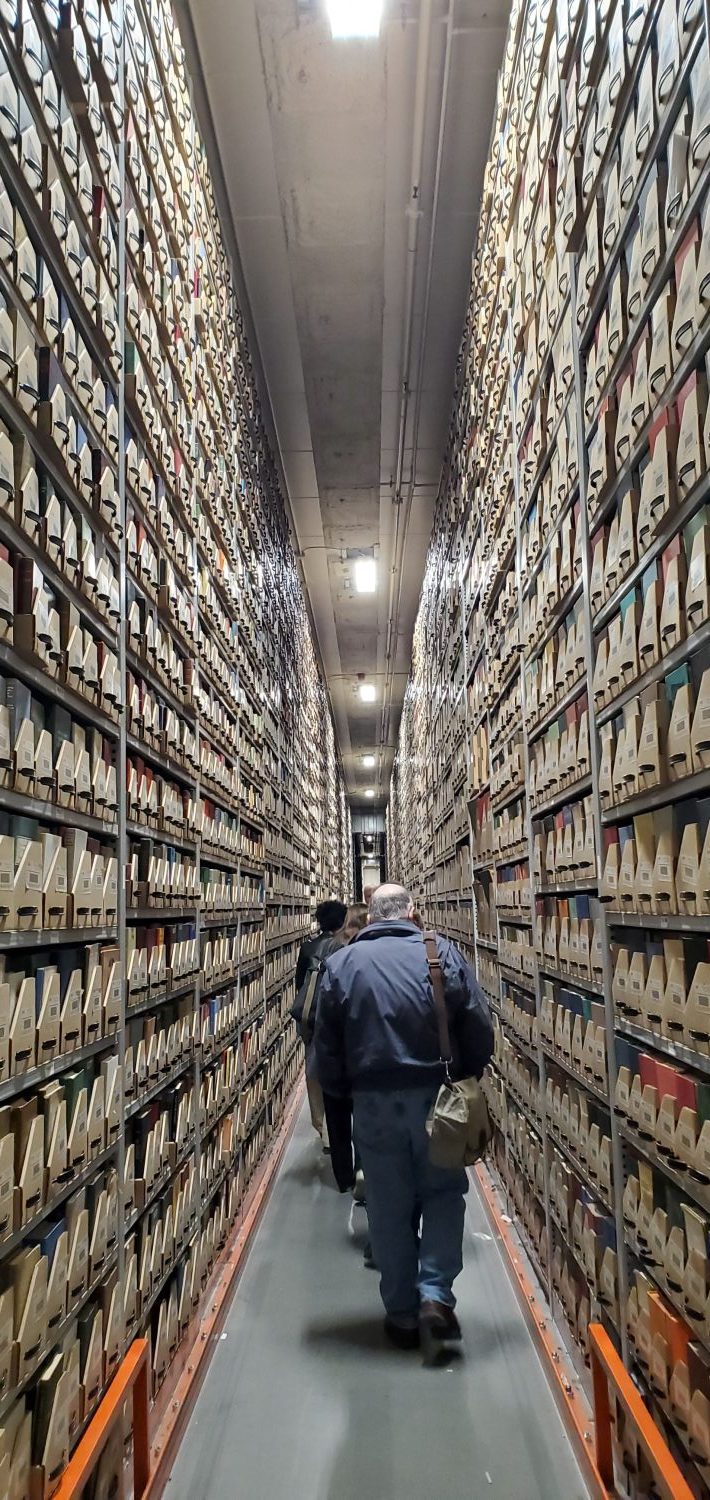 People walking between two high shelves packed with archival trays.