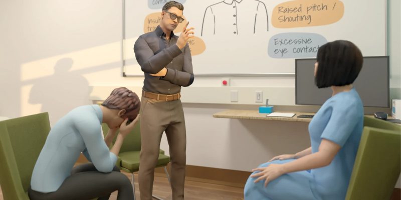 Individual standing talking to two sitting people, one showing signs of distress.