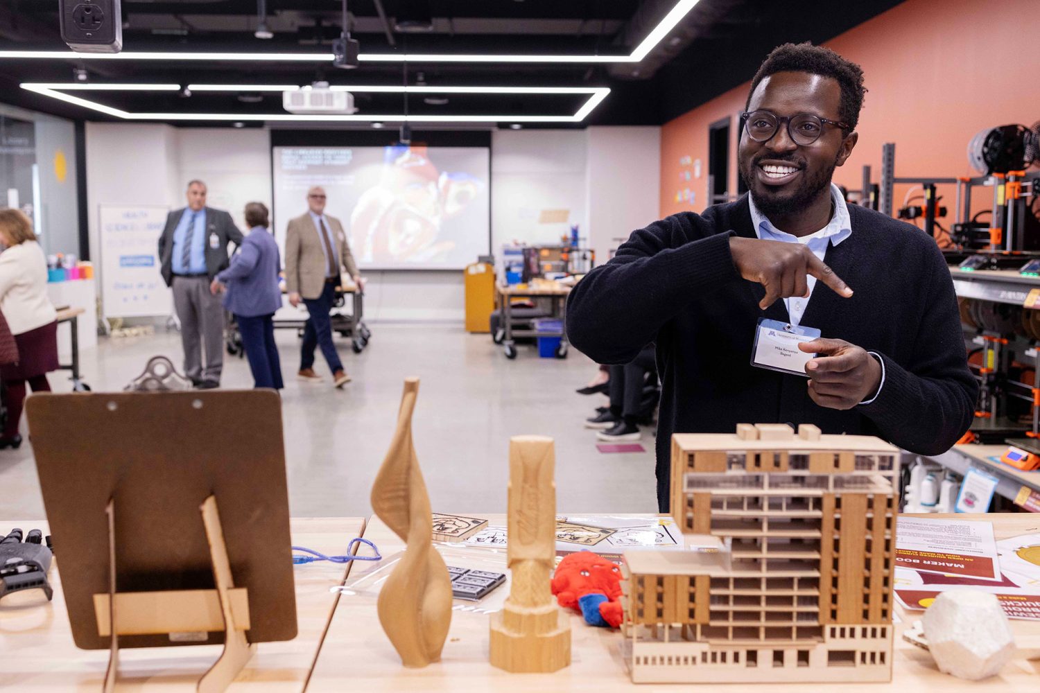 A smiling man stands in front of 3D printed objects in the Makerspace