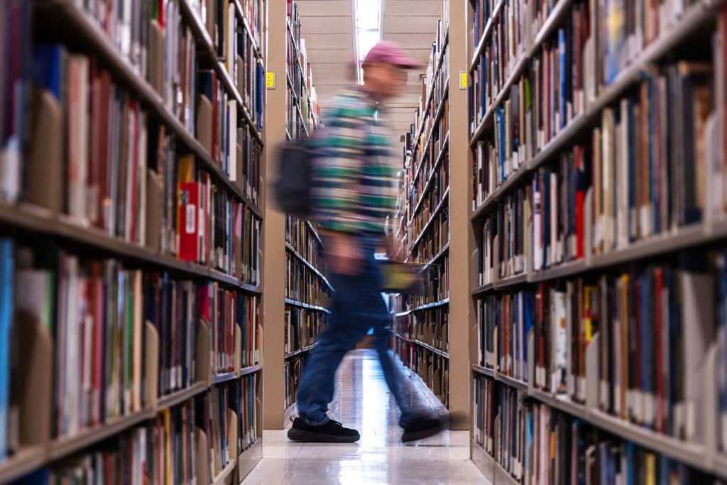 Intentionally blurred image of a student walking between aisles of stacks of books