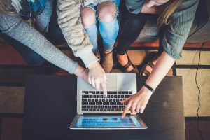From above, three people pointing to something on a laptop