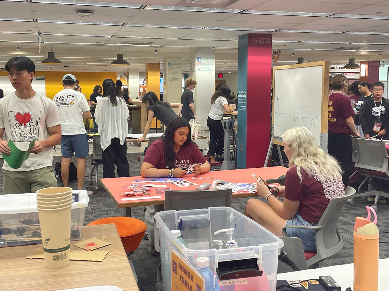 Room full of students in maroon welcome week t-shirts in the Toaster Innovation Hub working on crafts projects and talking
