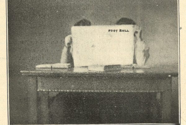 Image printed in an issue of the Ariel student newspaper depicting two students seated at a desk holding an issue of the publication FOOT BALL in front of their faces. The image includes the caption, "Studying Hard in Football Season."