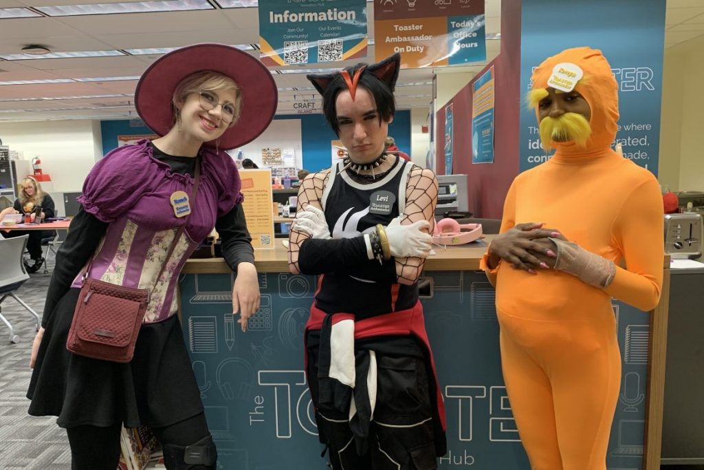 Three students in Halloween costumes. From left to right, they are dressed as: a witch, Shadow the Hedgehog, and the Lorax.