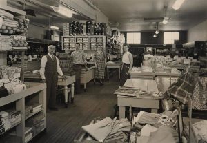 A black and white photograph of David Blumenfeld and three members of his staff stand in a stocked clothing store